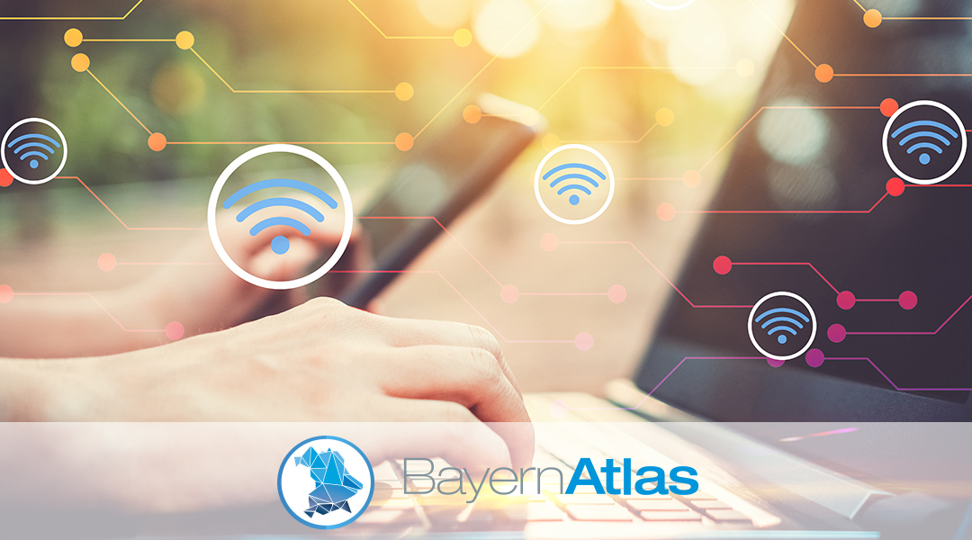 BayernAtlas-Thema BayernWLAN-Standorte Symbolbild: Zwei Hände mit Smartphone und Laptop, WLAN-Symbole und BayernAtlas-Logo im Vordergrund.