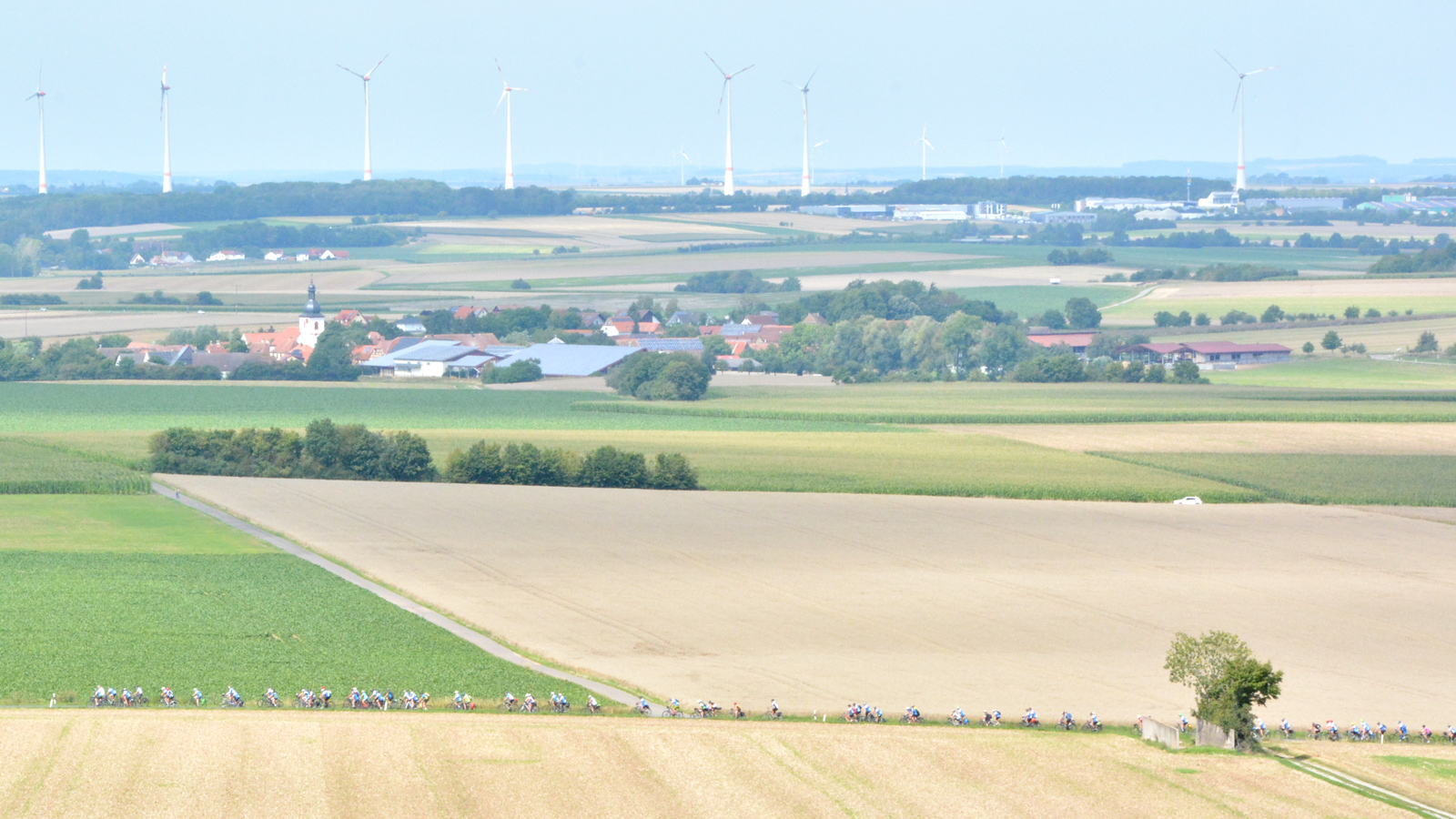 Impression der BR-Radltour 2025 Landschaft im Vordergrund ist klein eine Straße voll Radlerinnen und Radlern erkennbar